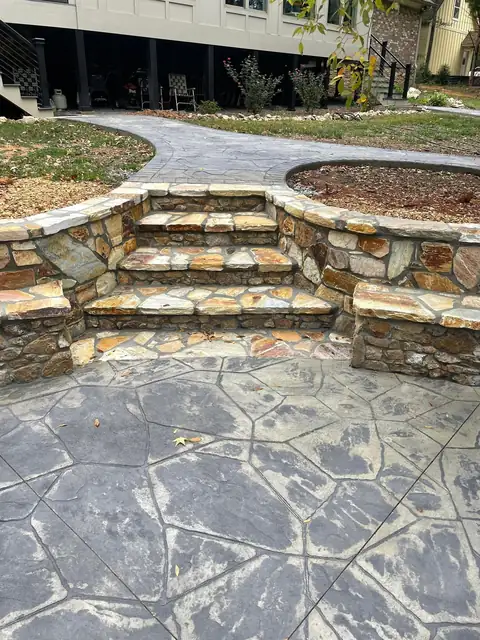 Stone steps and seating wall rising from a stamped concrete patio